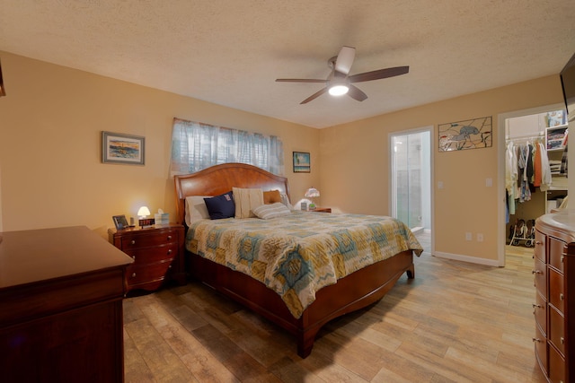 bedroom featuring light wood-type flooring, a textured ceiling, a closet, baseboards, and a spacious closet