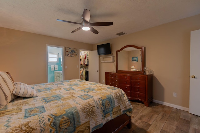 bedroom featuring a walk in closet, visible vents, a textured ceiling, wood finished floors, and baseboards