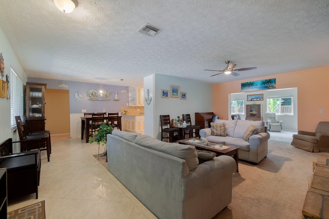 living area featuring light tile patterned floors, visible vents, a textured ceiling, and ceiling fan