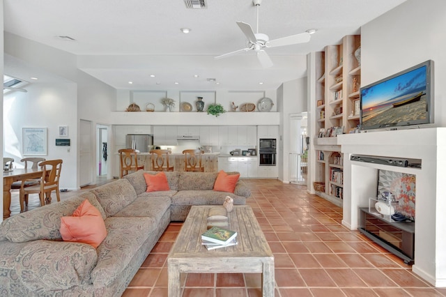 living area with visible vents, built in shelves, a ceiling fan, light tile patterned floors, and a towering ceiling