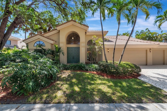 mediterranean / spanish home featuring a front lawn, a tiled roof, stucco siding, decorative driveway, and a garage