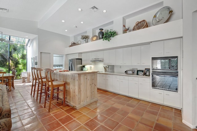 kitchen featuring visible vents, a center island, under cabinet range hood, a high ceiling, and black appliances