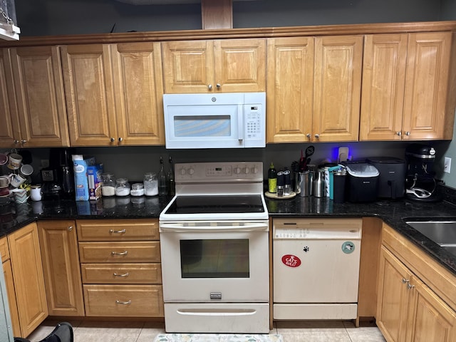 kitchen featuring dark stone countertops, white appliances, and light tile patterned flooring