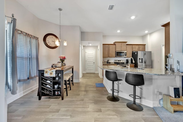 kitchen featuring visible vents, a kitchen bar, light stone counters, light wood-style flooring, and stainless steel appliances