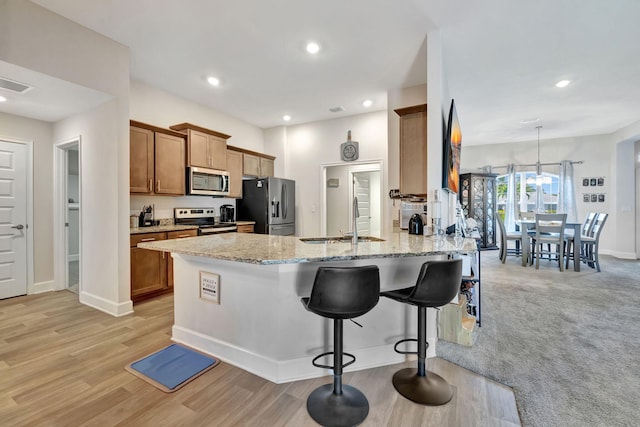 kitchen with visible vents, a breakfast bar, light stone counters, appliances with stainless steel finishes, and a sink