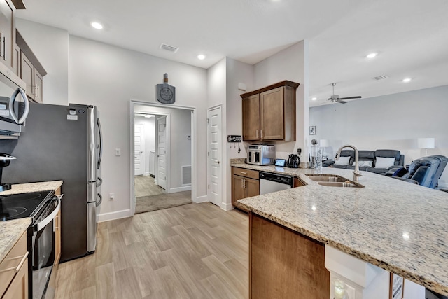 kitchen with light stone counters, light wood-style floors, stainless steel appliances, a ceiling fan, and a sink