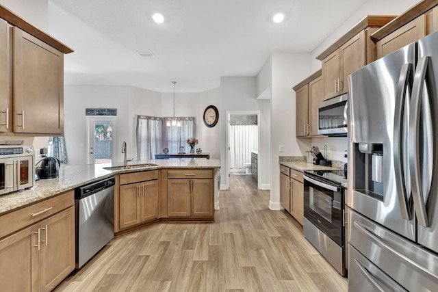 kitchen with light stone counters, a peninsula, light wood-style floors, stainless steel appliances, and a sink