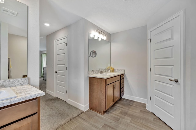 bathroom with wood finished floors, baseboards, visible vents, two vanities, and a sink