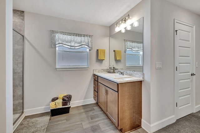 bathroom featuring baseboards, wood finished floors, vanity, and a tile shower