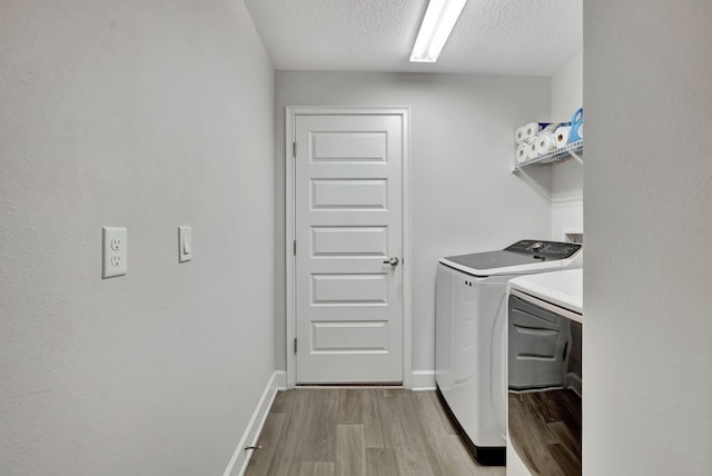 washroom with light wood-style flooring, washer and dryer, a textured ceiling, baseboards, and laundry area