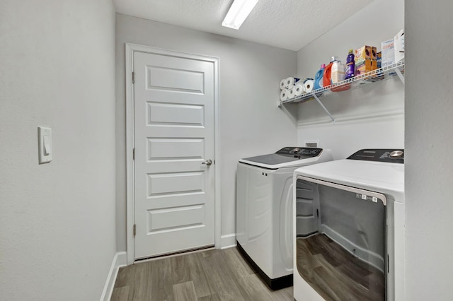 laundry room with light wood-type flooring, a textured ceiling, washing machine and dryer, baseboards, and laundry area