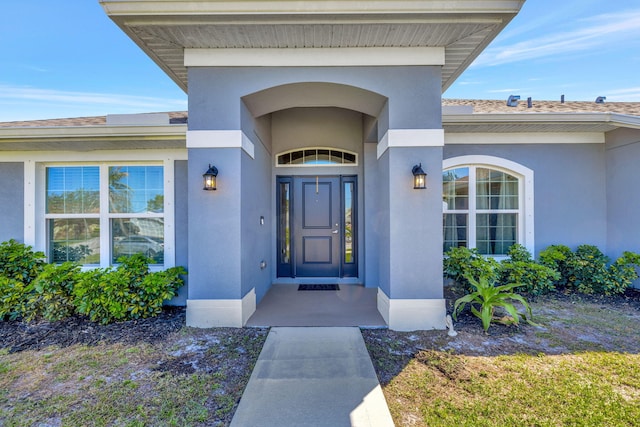 view of exterior entry featuring stucco siding and roof with shingles