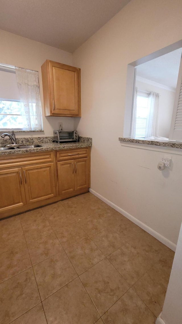 kitchen featuring baseboards, light stone countertops, a sink, and light tile patterned floors