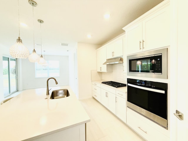 kitchen featuring a sink, light countertops, under cabinet range hood, appliances with stainless steel finishes, and backsplash