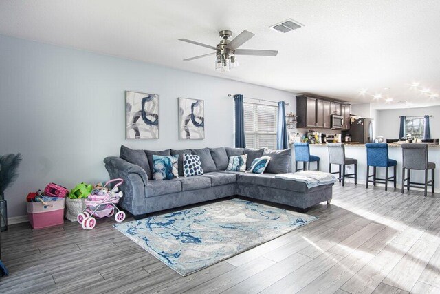 living room with visible vents, plenty of natural light, a ceiling fan, and wood finished floors