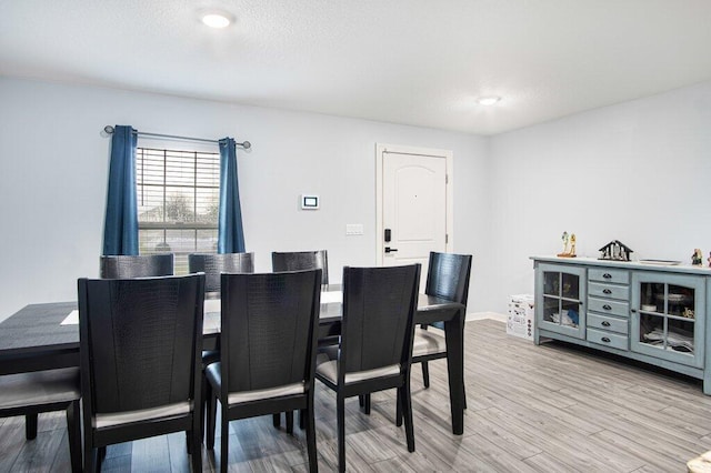 dining room featuring baseboards, light wood-style floors, and a textured ceiling