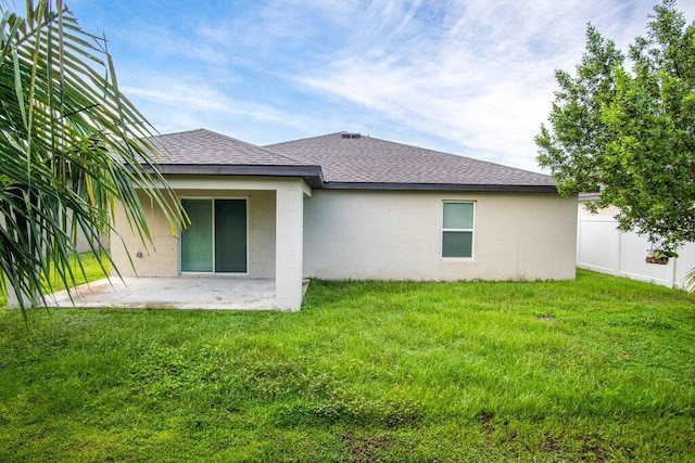 rear view of property with a patio area, a lawn, roof with shingles, and fence