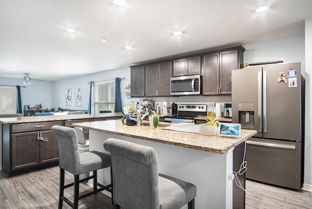 kitchen with light wood-style flooring, stainless steel appliances, a peninsula, light stone countertops, and dark brown cabinets