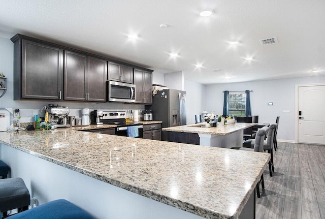 kitchen with visible vents, light stone counters, wood finished floors, a peninsula, and appliances with stainless steel finishes