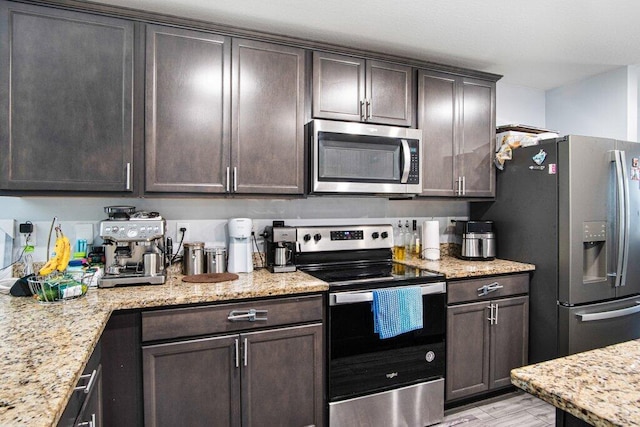 kitchen featuring light stone countertops, dark brown cabinetry, appliances with stainless steel finishes, and light wood finished floors