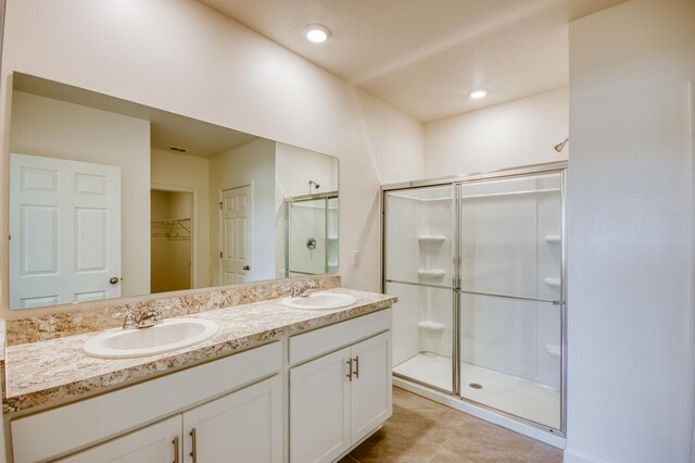 bathroom featuring double vanity, a spacious closet, a stall shower, and a sink