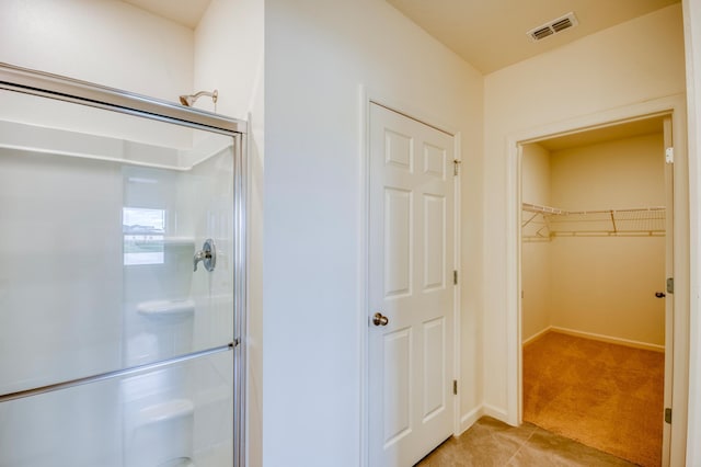 bathroom with a spacious closet, visible vents, a stall shower, and baseboards