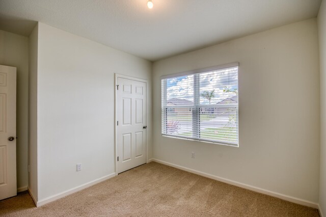 spare room featuring light colored carpet and baseboards