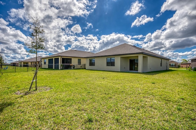 back of property featuring stucco siding, a sunroom, a yard, and fence