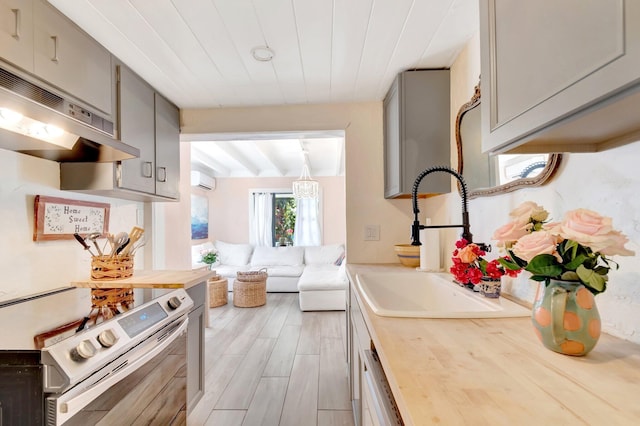 kitchen with gray cabinets, a sink, stainless steel range with electric cooktop, under cabinet range hood, and wood counters