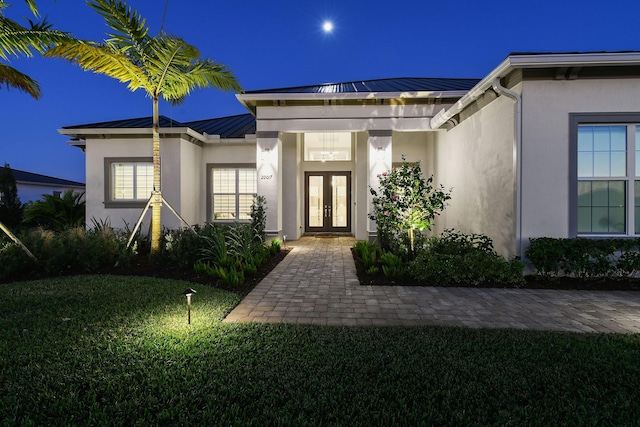 20017 SE Bridgewater Dr, Jupiter, FL 33458 - exterior entry at twilight featuring french doors, a standing seam roof, stucco siding, metal roof, and a lawn