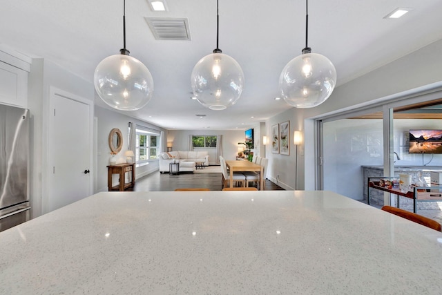 kitchen with decorative light fixtures, light stone countertops, visible vents, and freestanding refrigerator