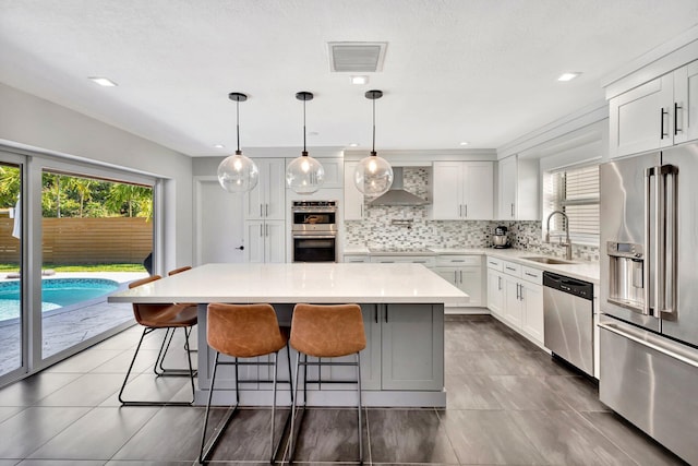 kitchen with visible vents, a sink, appliances with stainless steel finishes, wall chimney range hood, and decorative backsplash