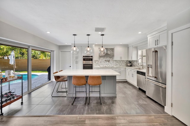 kitchen with a sink, wall chimney range hood, tasteful backsplash, appliances with stainless steel finishes, and light countertops