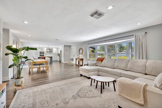 living area featuring visible vents, recessed lighting, a textured ceiling, and wood finished floors