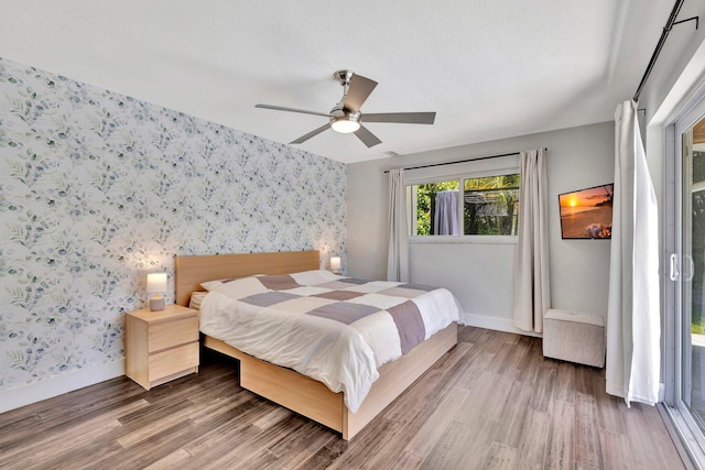 bedroom featuring wallpapered walls, an accent wall, baseboards, and wood finished floors