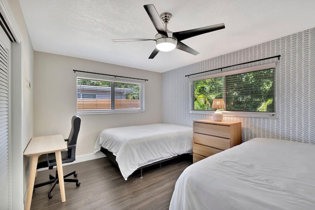 bedroom with wallpapered walls, baseboards, wood finished floors, a textured ceiling, and a ceiling fan