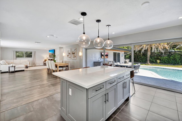 kitchen with tile patterned flooring, a kitchen island, open floor plan, light countertops, and gray cabinets