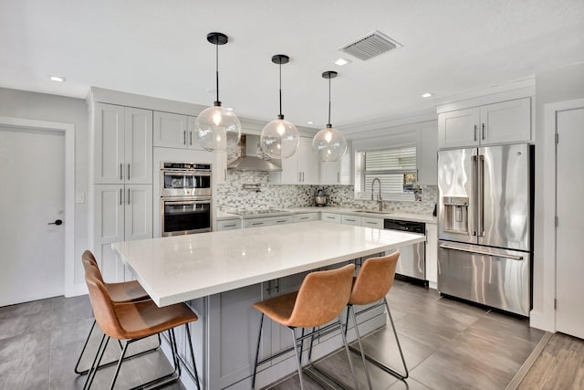 kitchen featuring visible vents, wall chimney range hood, backsplash, stainless steel appliances, and light countertops