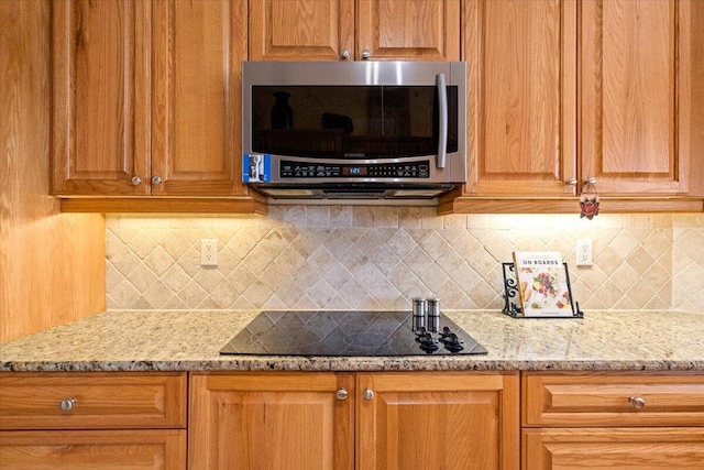 kitchen featuring light stone counters, stainless steel microwave, black electric cooktop, and decorative backsplash