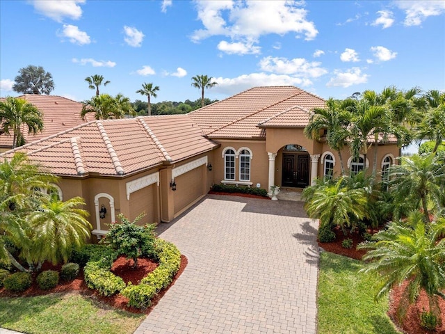 mediterranean / spanish house featuring a garage, decorative driveway, stucco siding, and a tiled roof