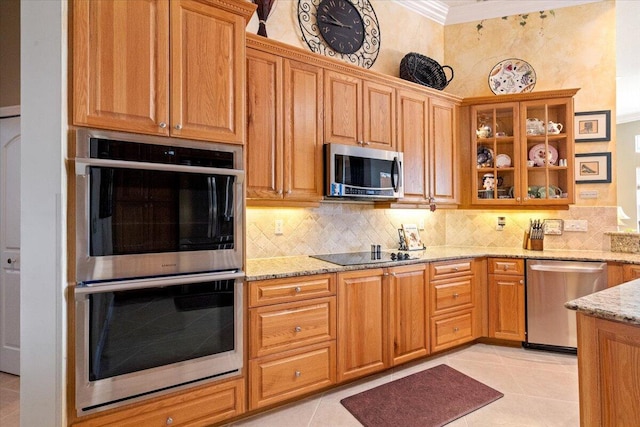 kitchen featuring glass insert cabinets, crown molding, light stone countertops, decorative backsplash, and appliances with stainless steel finishes