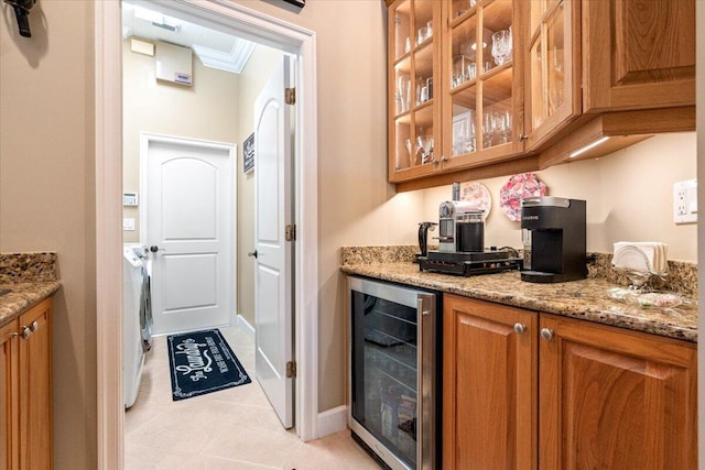 kitchen featuring beverage cooler, light stone counters, washer and dryer, brown cabinetry, and glass insert cabinets