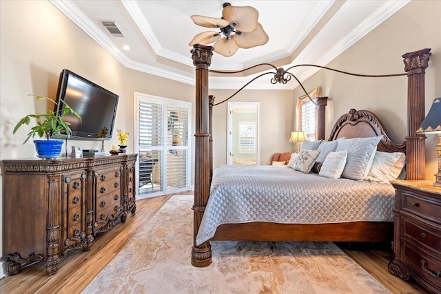 bedroom with light wood finished floors, visible vents, a raised ceiling, and ornamental molding