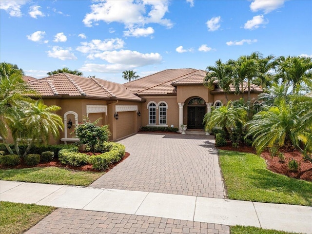 mediterranean / spanish house with stucco siding, an attached garage, a tile roof, and decorative driveway