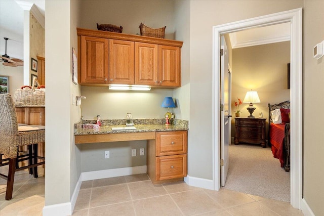 kitchen with light stone counters, light tile patterned floors, a ceiling fan, and built in desk