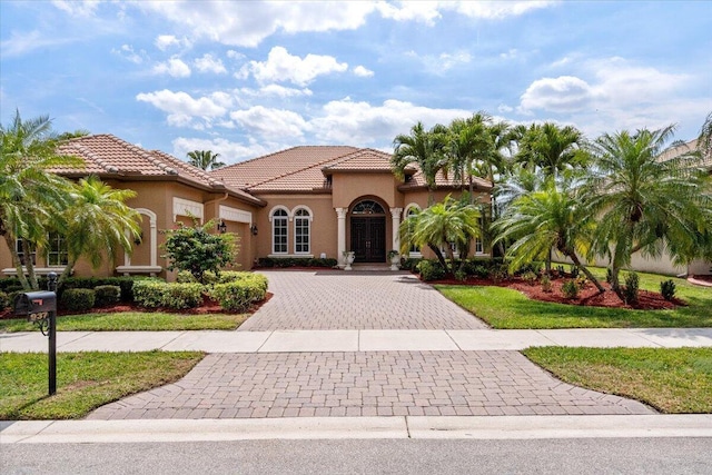 mediterranean / spanish home featuring decorative driveway, a tile roof, an attached garage, and stucco siding