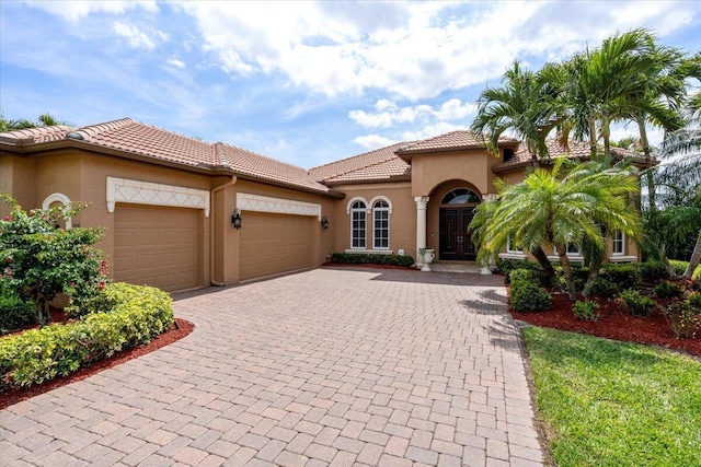 mediterranean / spanish-style home with a tiled roof, a garage, driveway, and stucco siding