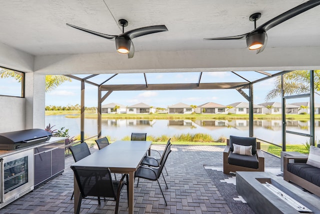 view of patio featuring a water view, an outdoor kitchen, glass enclosure, a grill, and ceiling fan