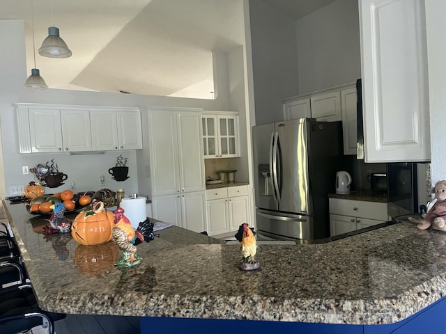 kitchen featuring a breakfast bar area, dark stone countertops, a peninsula, stainless steel fridge, and white cabinetry