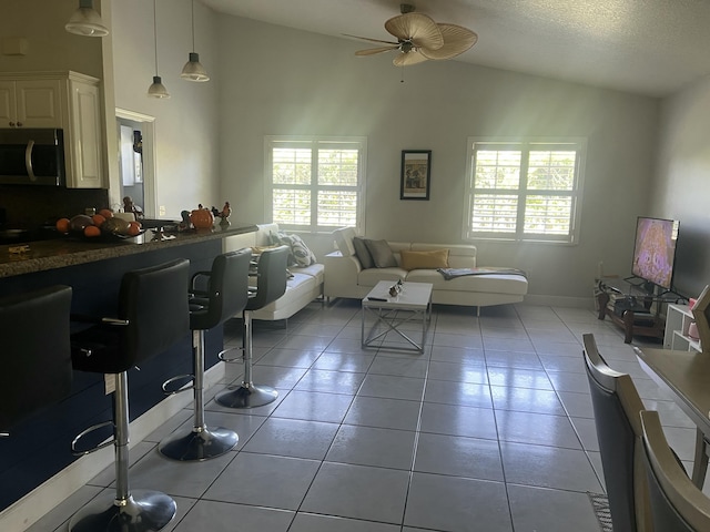 living area featuring baseboards, ceiling fan, vaulted ceiling, light tile patterned floors, and a textured ceiling